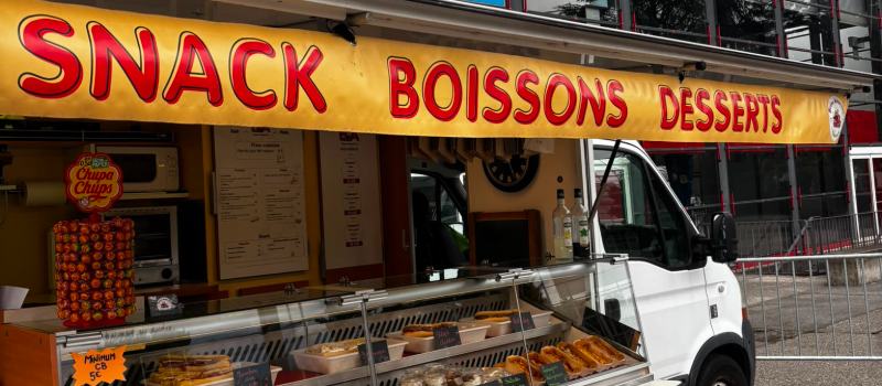Le comptoir du camion ouvert : auvent « Snack Boissons Desserts » et vitrine réfrigérée garnie de paninis, salades, tiramisus et gâteaux.