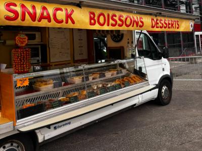 Le comptoir du camion ouvert : auvent « Snack Boissons Desserts » et vitrine réfrigérée garnie de paninis, salades, tiramisus et gâteaux.