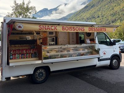 Le camion Buena Aventura, auvent « Snack Boissons Desserts » déployé et vitrine garnie, garé au pied des montagnes.