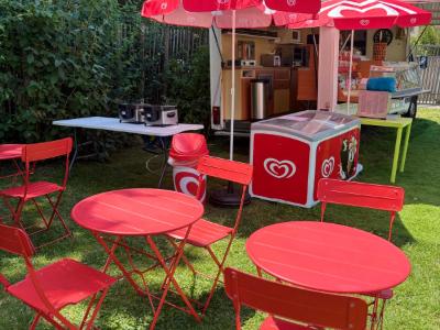 La terrasse du camion : tables rondes et chaises rouges à l’ombre.